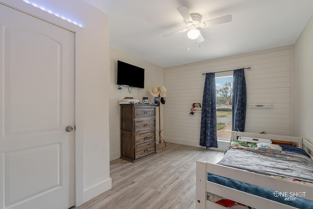 bedroom with ceiling fan, light hardwood / wood-style flooring, and wood walls