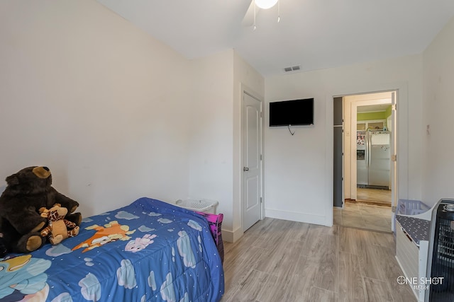 bedroom featuring hardwood / wood-style flooring, ceiling fan, and stainless steel refrigerator with ice dispenser