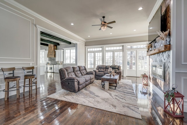 living room with crown molding, ceiling fan, dark wood-type flooring, and a stone fireplace