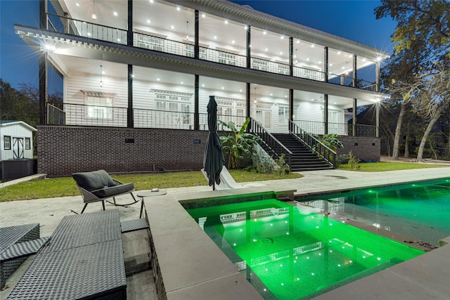 back house at night featuring a swimming pool with hot tub, a balcony, and a patio