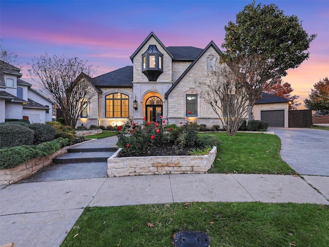 view of front facade featuring a garage, stone siding, driveway, and a lawn