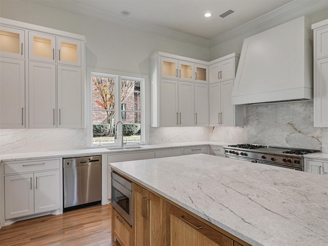 kitchen featuring white cabinets, sink, light stone counters, custom range hood, and stainless steel appliances