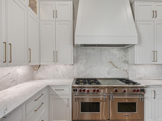 kitchen with white cabinetry, light stone countertops, tasteful backsplash, range with two ovens, and custom range hood