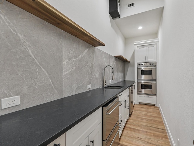 kitchen featuring backsplash, sink, white cabinetry, light hardwood / wood-style floors, and stainless steel double oven