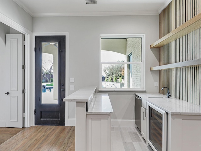 interior space featuring sink, beverage cooler, kitchen peninsula, light wood-type flooring, and ornamental molding