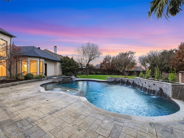 pool at dusk featuring pool water feature, a patio area, a yard, and an in ground hot tub