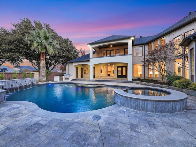 pool at dusk with an in ground hot tub, area for grilling, pool water feature, and a patio