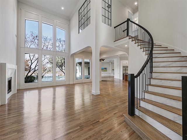 unfurnished living room with a premium fireplace, hardwood / wood-style floors, crown molding, and a high ceiling