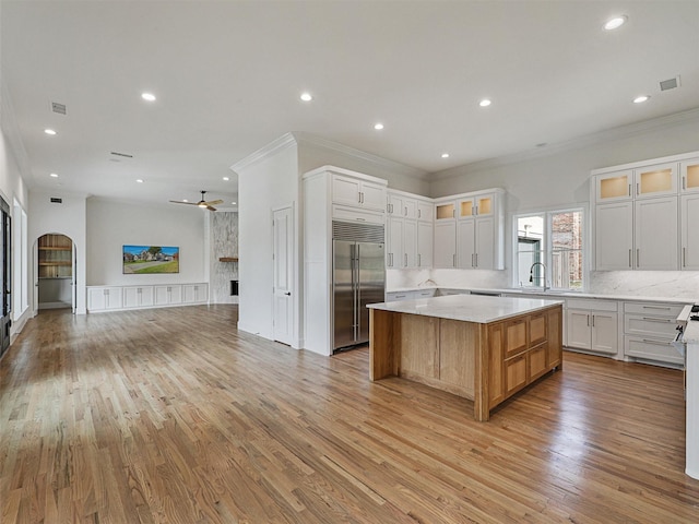 kitchen with built in refrigerator, white cabinets, a spacious island, and light wood-type flooring