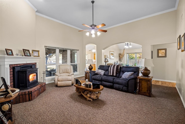 carpeted living room featuring ceiling fan, a wood stove, crown molding, and a high ceiling