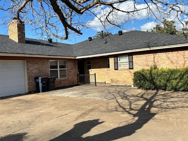 exterior space featuring brick siding, an attached garage, a chimney, and a shingled roof