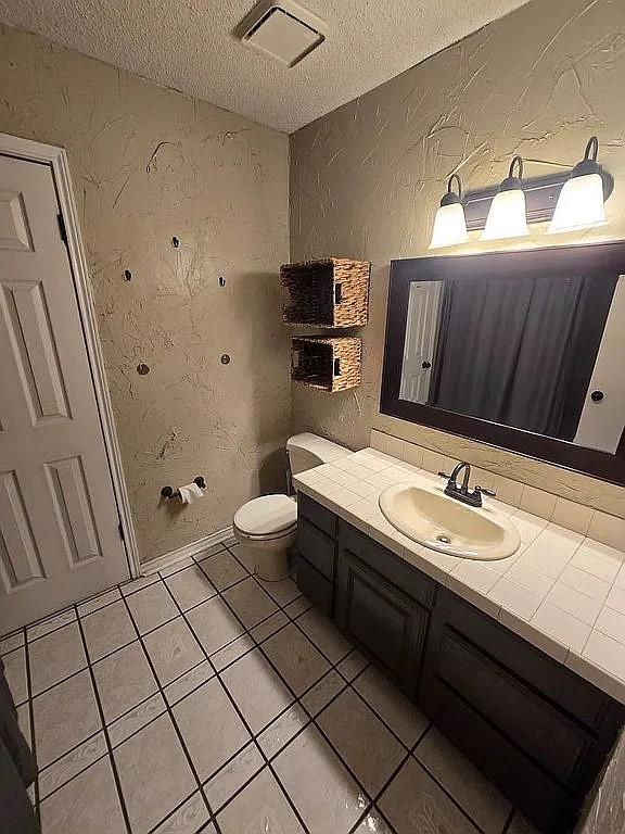 bathroom featuring tile patterned flooring, vanity, a textured ceiling, and toilet