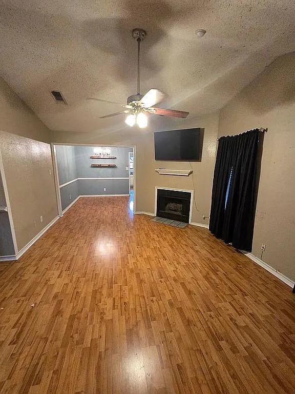 unfurnished living room featuring lofted ceiling, ceiling fan, a textured ceiling, and hardwood / wood-style flooring