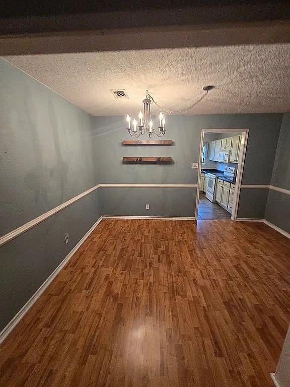 unfurnished dining area with dark hardwood / wood-style flooring, a textured ceiling, and an inviting chandelier