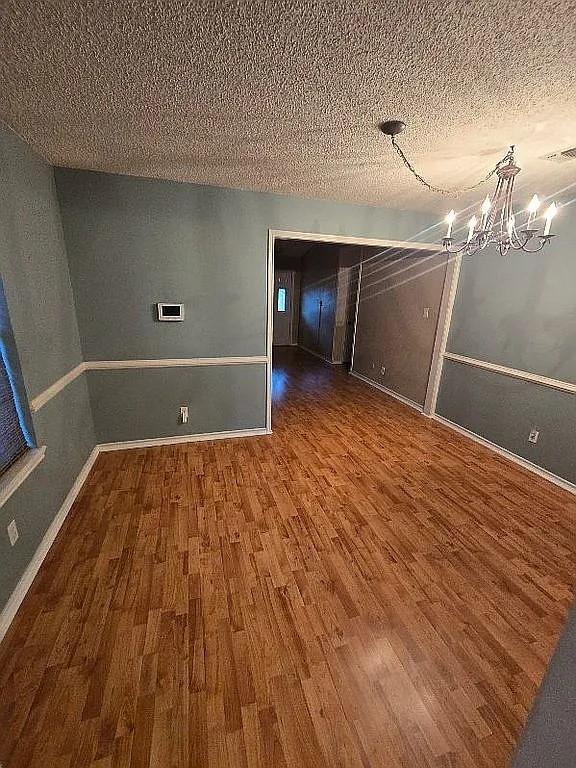 unfurnished room with dark hardwood / wood-style floors, a textured ceiling, and an inviting chandelier