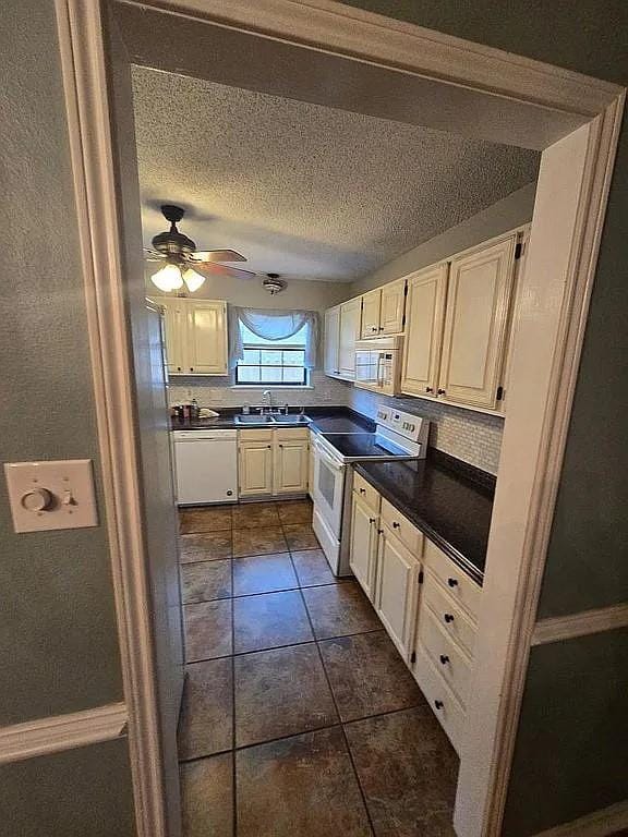 kitchen with a textured ceiling, white appliances, ceiling fan, sink, and white cabinetry