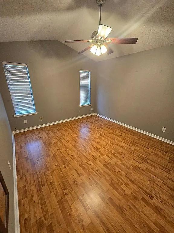 empty room with ceiling fan, lofted ceiling, a textured ceiling, and light hardwood / wood-style floors