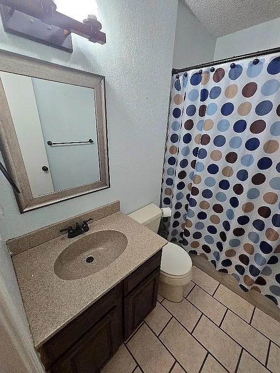 bathroom with tile patterned flooring, vanity, a textured ceiling, and toilet