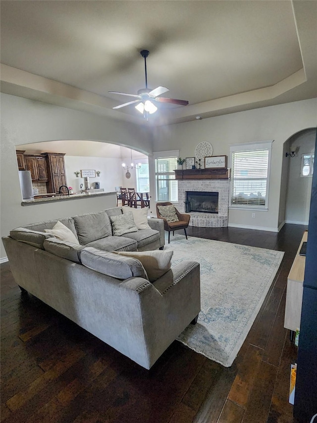 living room featuring a fireplace, ceiling fan with notable chandelier, dark hardwood / wood-style floors, and a healthy amount of sunlight