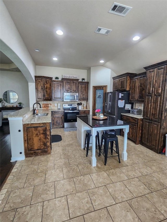 kitchen with dark brown cabinetry, sink, backsplash, kitchen peninsula, and appliances with stainless steel finishes