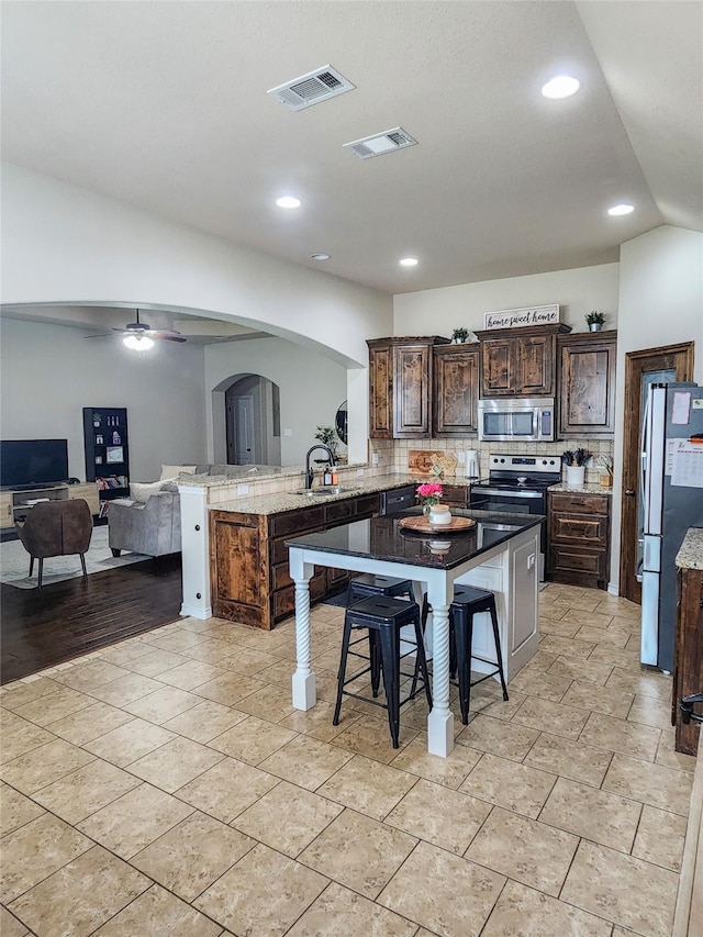 kitchen with kitchen peninsula, a breakfast bar area, ceiling fan, dark brown cabinetry, and stainless steel appliances