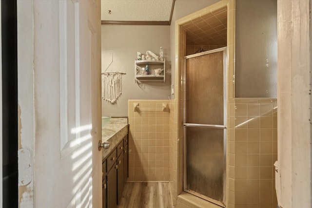 bathroom featuring wood-type flooring, tile walls, vanity, walk in shower, and a textured ceiling