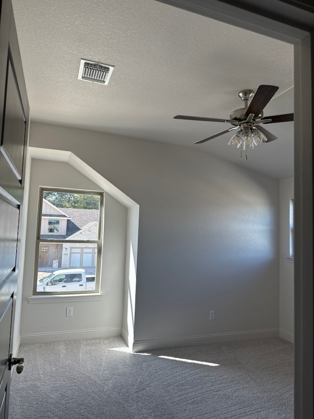 unfurnished room featuring carpet flooring, ceiling fan, vaulted ceiling, and a textured ceiling