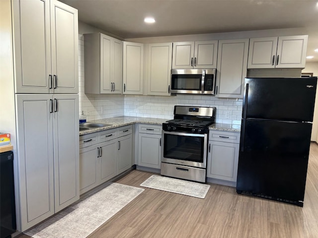 kitchen with light hardwood / wood-style flooring, gray cabinets, backsplash, light stone countertops, and black appliances