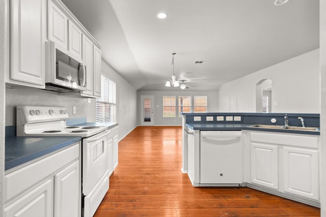 kitchen with white appliances, wood-type flooring, sink, vaulted ceiling, and white cabinetry