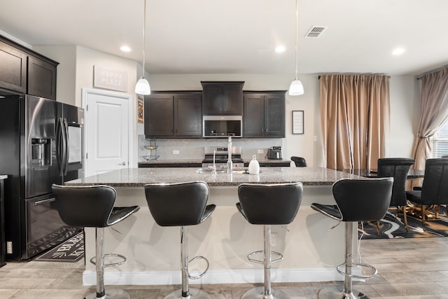 kitchen with appliances with stainless steel finishes, a kitchen island with sink, backsplash, a kitchen bar, and decorative light fixtures