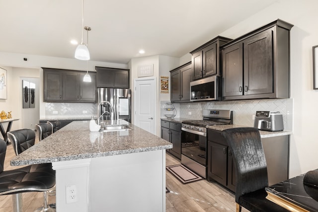 kitchen with sink, hanging light fixtures, appliances with stainless steel finishes, a kitchen breakfast bar, and a kitchen island with sink