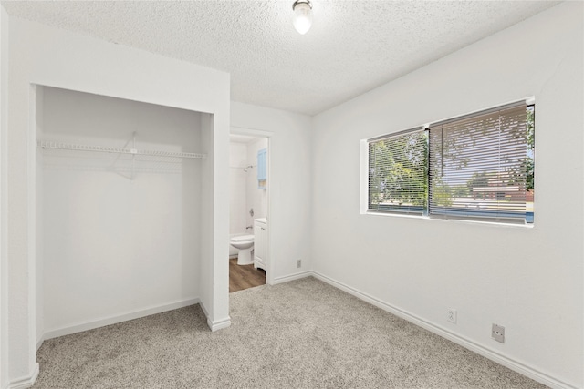 unfurnished bedroom featuring a textured ceiling, carpet floors, ensuite bath, and a closet