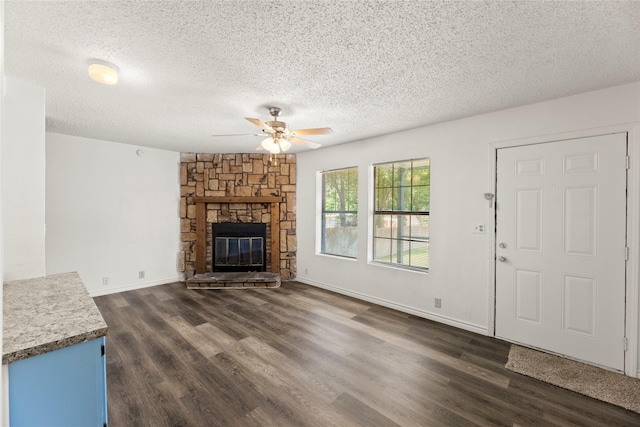 unfurnished living room featuring a stone fireplace, dark wood-type flooring, a textured ceiling, and ceiling fan