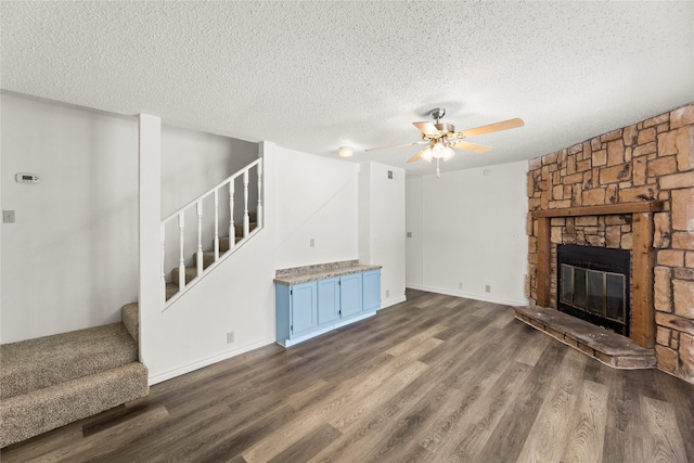 unfurnished living room featuring a textured ceiling, a stone fireplace, ceiling fan, and dark wood-type flooring