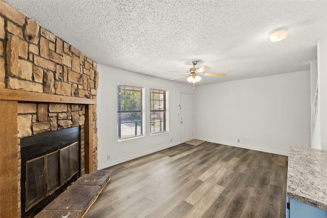 unfurnished living room featuring a textured ceiling, dark hardwood / wood-style flooring, a stone fireplace, and ceiling fan