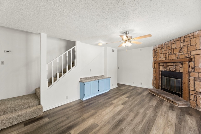 137 Montego Dr, Mesquite, TX 75149 - unfurnished living room featuring stairs, dark wood-style floors, ceiling fan, a textured ceiling, and a stone fireplace