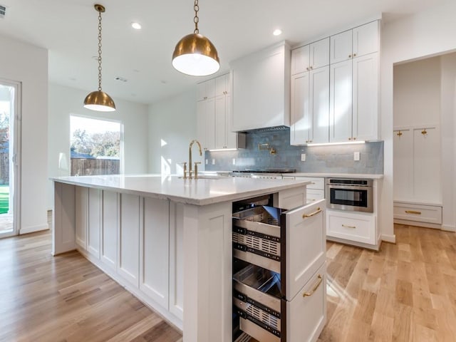 kitchen with premium range hood, sink, white cabinets, light hardwood / wood-style floors, and an island with sink