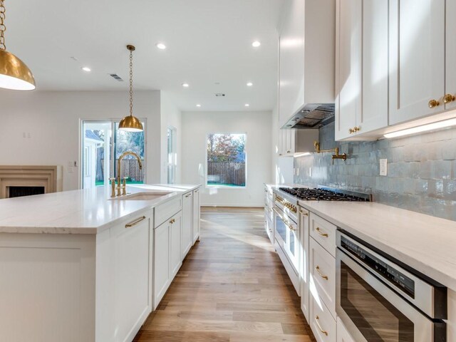 kitchen featuring pendant lighting, custom exhaust hood, a center island with sink, high end stove, and white cabinetry