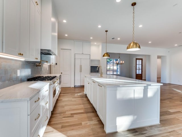 kitchen with a spacious island, decorative light fixtures, high quality appliances, white cabinets, and light hardwood / wood-style floors