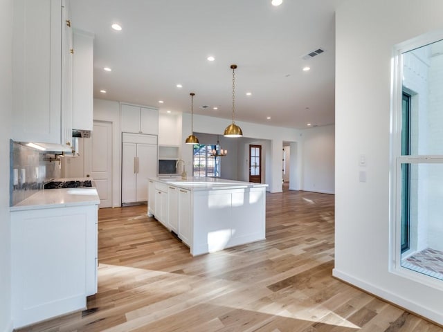 kitchen featuring paneled built in refrigerator, light hardwood / wood-style floors, decorative light fixtures, a kitchen island with sink, and white cabinets