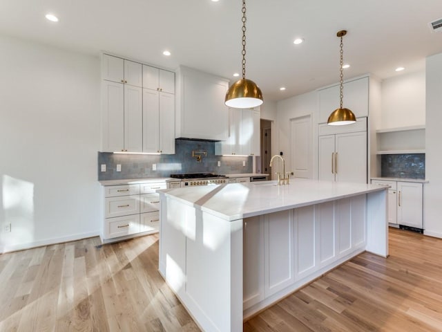 kitchen with a large island with sink, white cabinetry, light hardwood / wood-style flooring, and paneled refrigerator