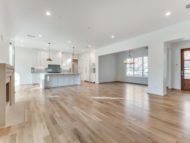 unfurnished living room with a wealth of natural light, light hardwood / wood-style flooring, and a notable chandelier