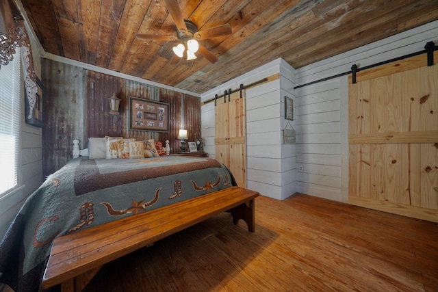 bedroom with hardwood / wood-style floors, wooden walls, ceiling fan, a barn door, and wood ceiling