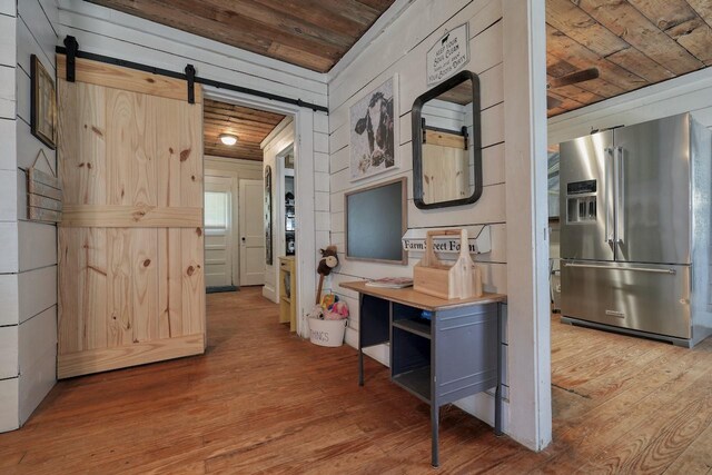 hall featuring a barn door, wooden walls, wooden ceiling, and light wood-type flooring