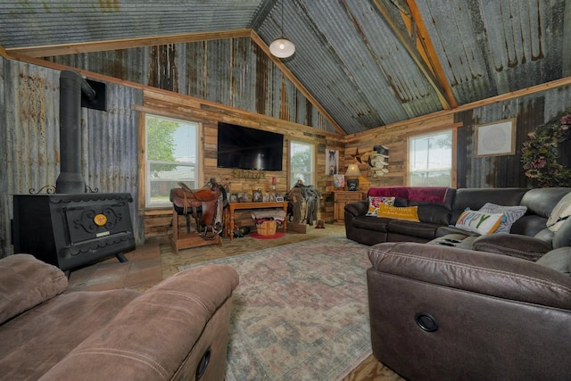 living room with wooden walls, plenty of natural light, a wood stove, and high vaulted ceiling