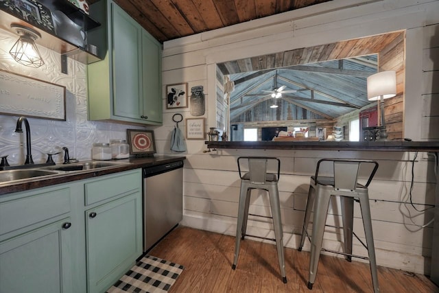 kitchen featuring ceiling fan, sink, stainless steel dishwasher, vaulted ceiling, and wooden walls