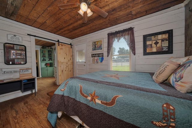 bedroom featuring wooden walls, hardwood / wood-style flooring, ceiling fan, a barn door, and wood ceiling