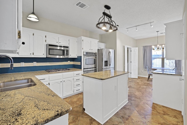 kitchen with stainless steel appliances, sink, pendant lighting, white cabinetry, and a kitchen island