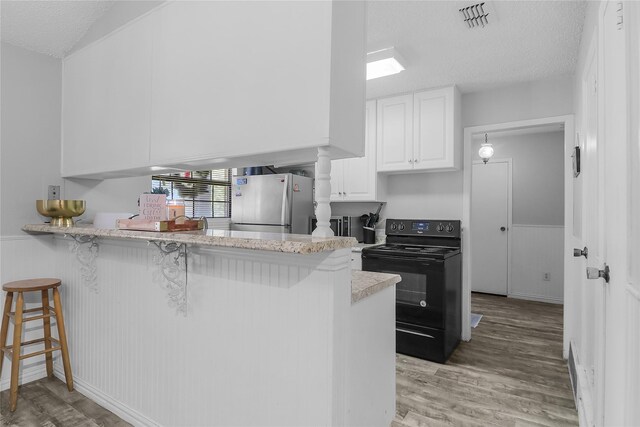 kitchen with white cabinetry, black electric range, kitchen peninsula, stainless steel fridge, and a breakfast bar area