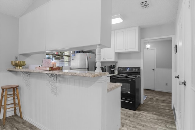 kitchen featuring a breakfast bar, black electric range oven, stainless steel refrigerator, kitchen peninsula, and white cabinets